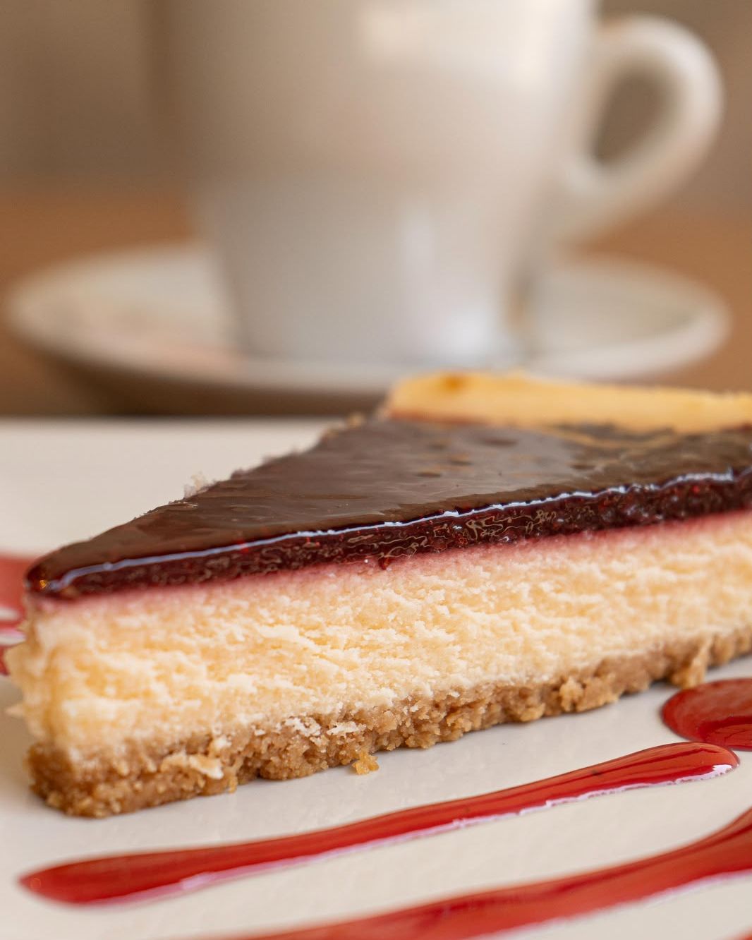 Porción de tarta de queso con cobertura de frutos rojos y un café detrás